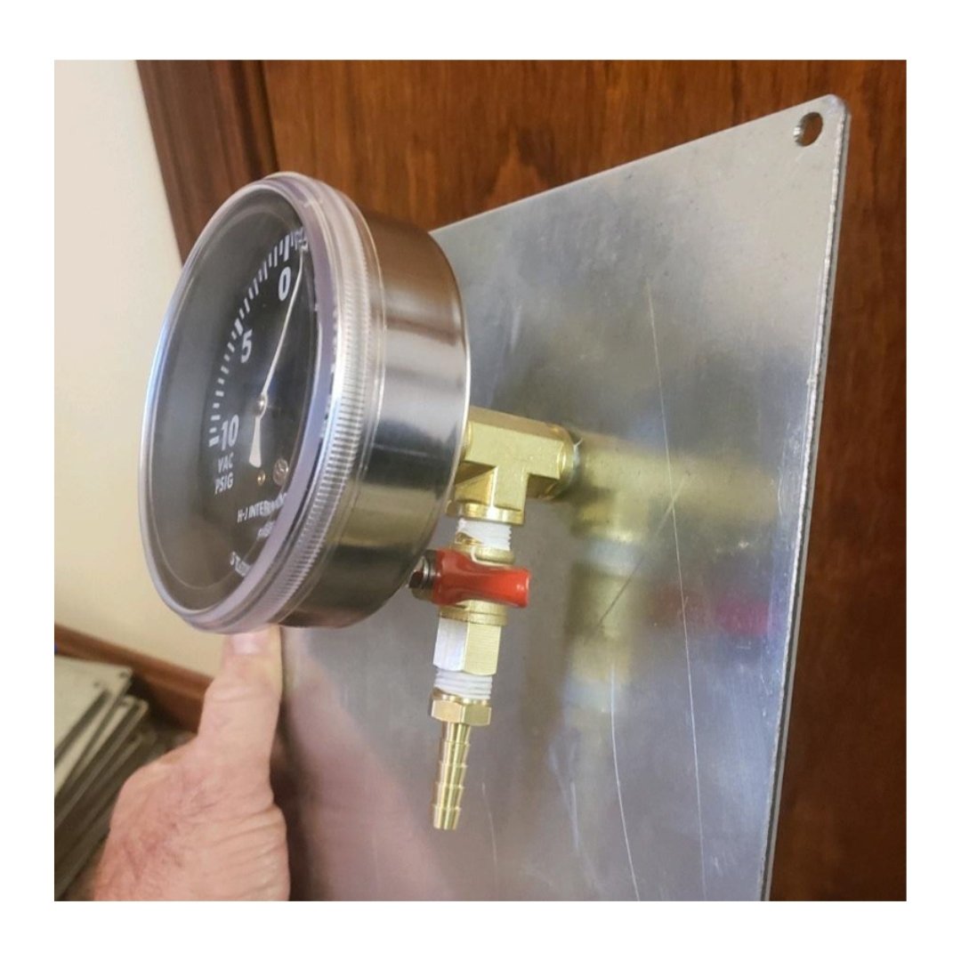 Technician holding the Extend-O-Valve assembly — vacuum gauge, brass T-fittings, red ball valve, and mounting plate